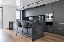 04 The kitchen is done with matte grey cabinets, a grey marble kitchen island, matte black chairs and a glass backsplash