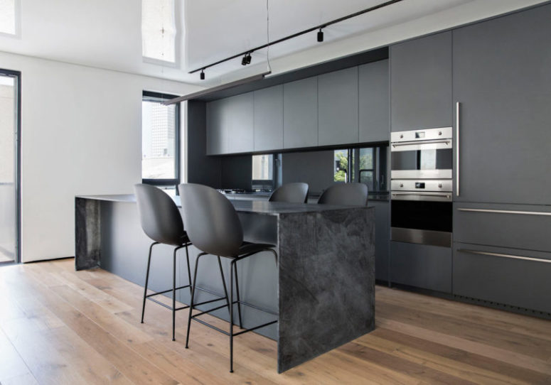 The kitchen is done with matte grey cabinets, a grey marble kitchen island, matte black chairs and a glass backsplash