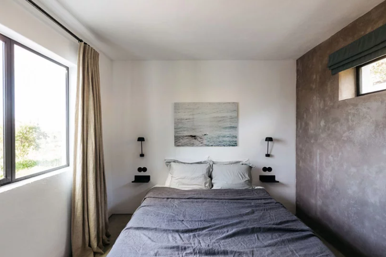 The bedroom is small yet peaceful, with a concrete wall, stylish bedding and an artwork
