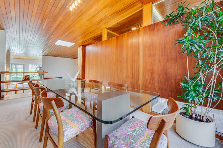 The dining room is done with colorful chairs and a glass dining table and there's a glazed wall for views and light