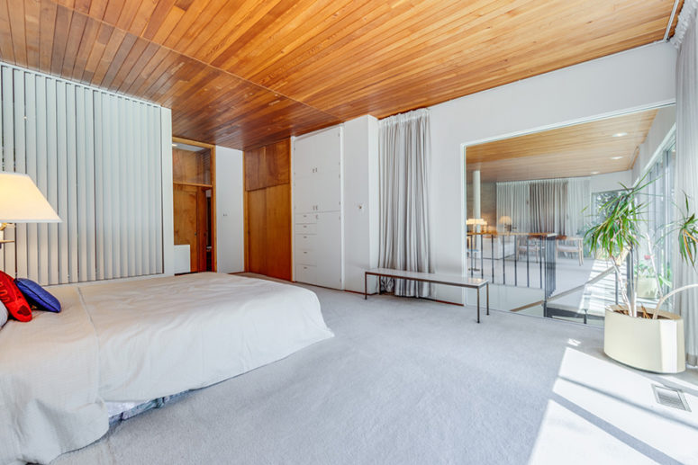 The master bedroom is done in off-whites, with built-in furniture and a large window to other spaces