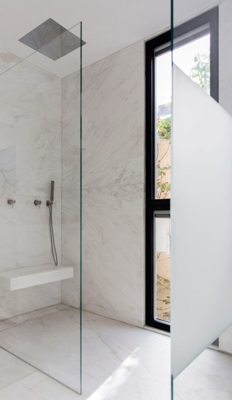 The bathroom is minimalist, done in white marble, with a seamless shower and a floor to ceiling window for a view and much light