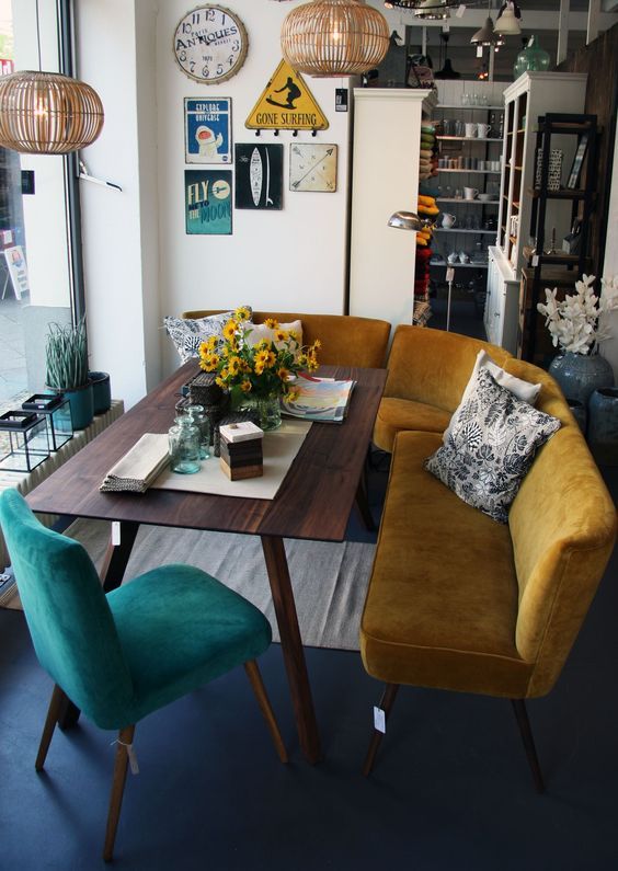 a curved mustard bench and a teal chair are paired to create a cozy mid-century modern breakfast nook