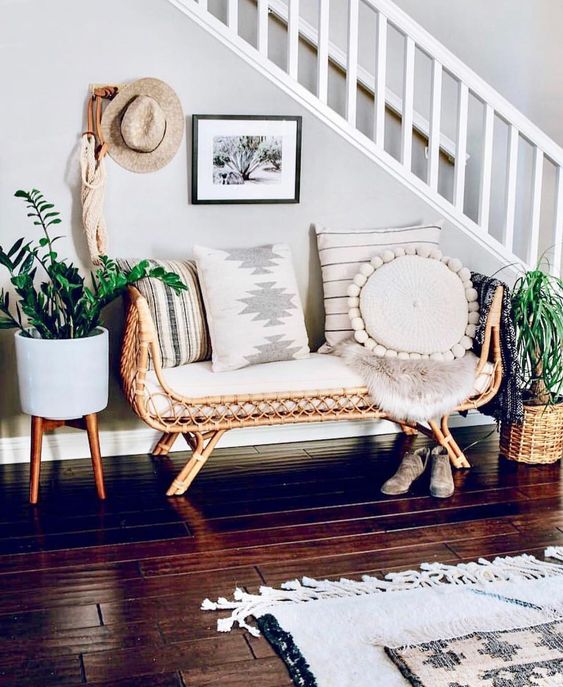 a boho summer entryway with a rattan bench, planters with greenery on stands, a straw hat and a boho rug