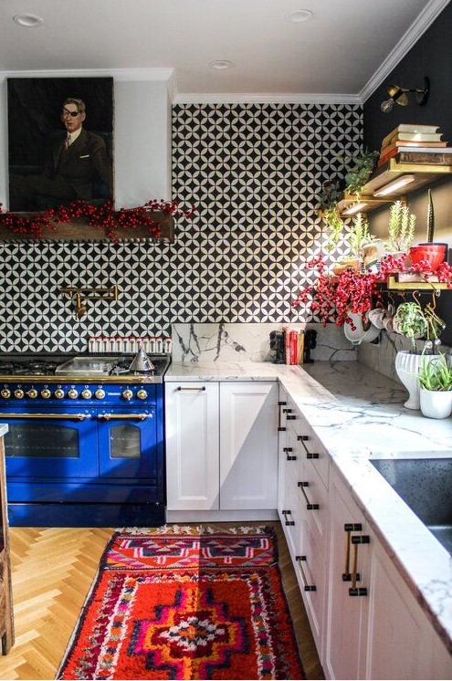a bold eclectic kitchen with white shaker style cabinets, a bold blue cooker, a bright rug, a black and white tile backsplash and a portrait