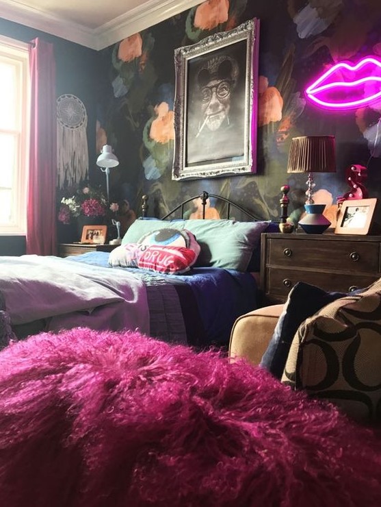 a bold maximalist bedroom with a dark floral accent wall, a metal bed, mid-century modern dressers, bold bedding and a neon light