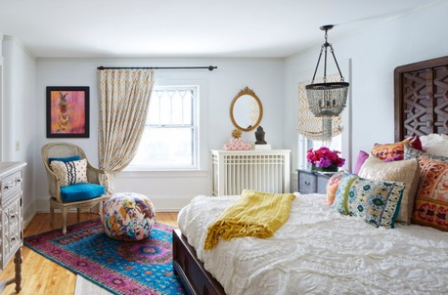 a bright eclectic bedroom done with colorful printed textiles, a modern wooden bed, a boho chandelier and some carved dressers
