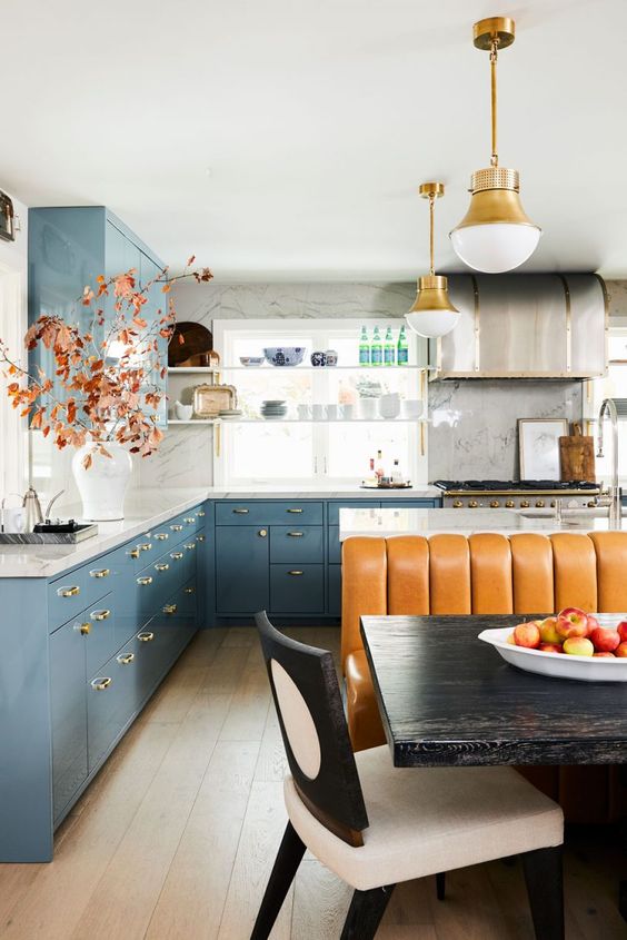 a bright eclectic kitchen with dusty blue cabinets, white marble countertops, a kitchen island, an amber leather sofa, pendant lamps