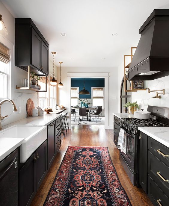 a chic black galley kitchen with white countertops and brass touches plus a printed rug and vintage pendant lamps