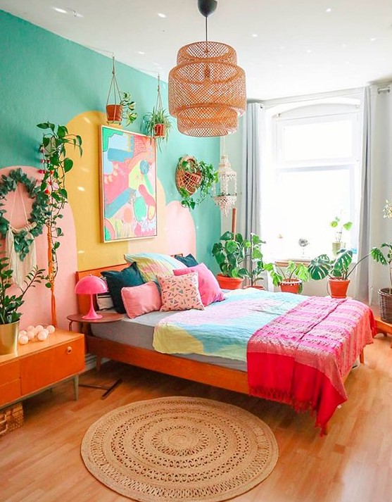 a colorful eclectic bedroom with an emerald accent wall, a red bed with colorful bedding, a bright artwork, potted plants, an orange credenza