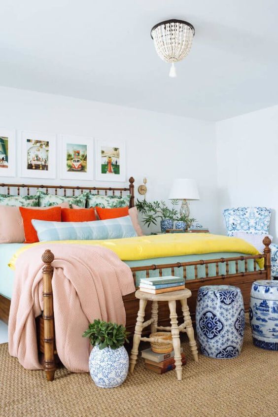 a colorful eclectic sleeping space with a bamboo bed, a gallery wall with holiday photos, elegant blue and white side tables and a bead chandelier