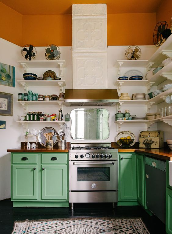 a colorful vintage meets rustic kitchen with a tiled hood, a rust stripe, green cabinets and white shelves