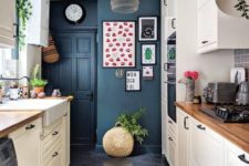 a contemporary kitchen with navy walls, white cabinets with wooden countertops and a catchy pendant lamp