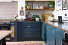 a contemporary meets boho kitchen with a boho rug, navy cabinets, a stone countertop and potted plants