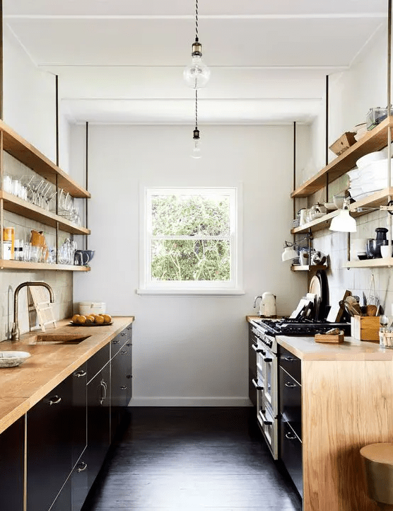 a contrasting galley kitchen with black cabinets, stained countertops, open shelves, some decor and brass fixtures