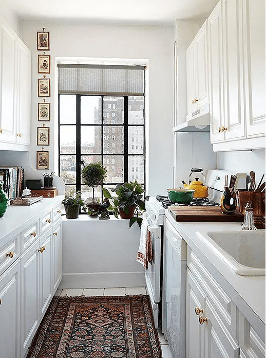 a cool galley kitchen with white cabinets, a boho rug, potted greenery, a gallery wall and some bright touches