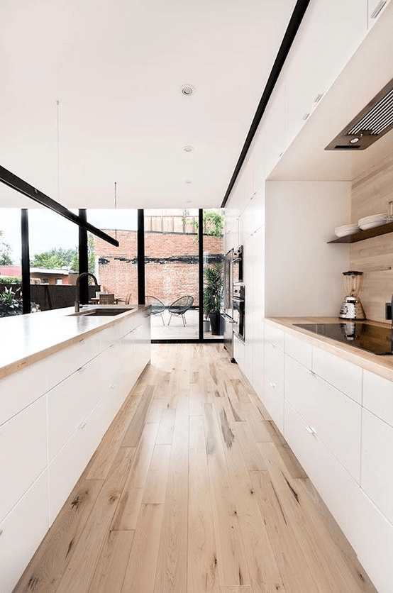 a cozy minimalist galley kitchen in white, with light-colored wooden countertops and a floor plus a backsplash, with glazed walls for more light