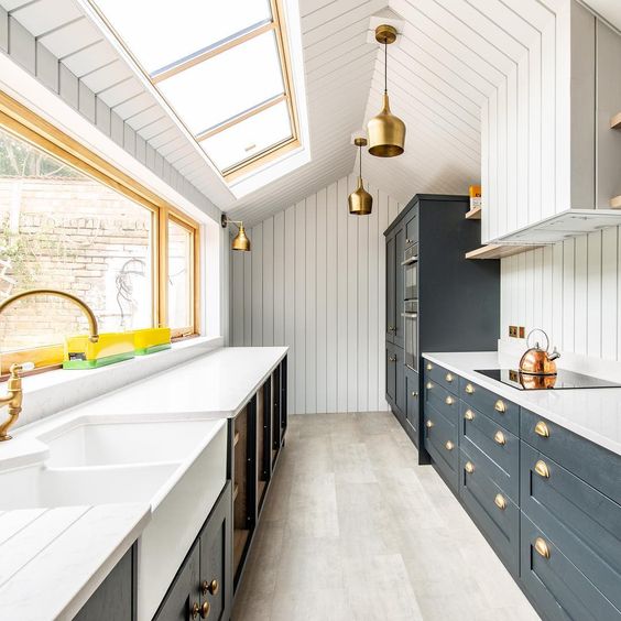 a farmhouse galley kitchen with navy and graphite grey cabinets, white stone countertops and much natural light coming through the windows