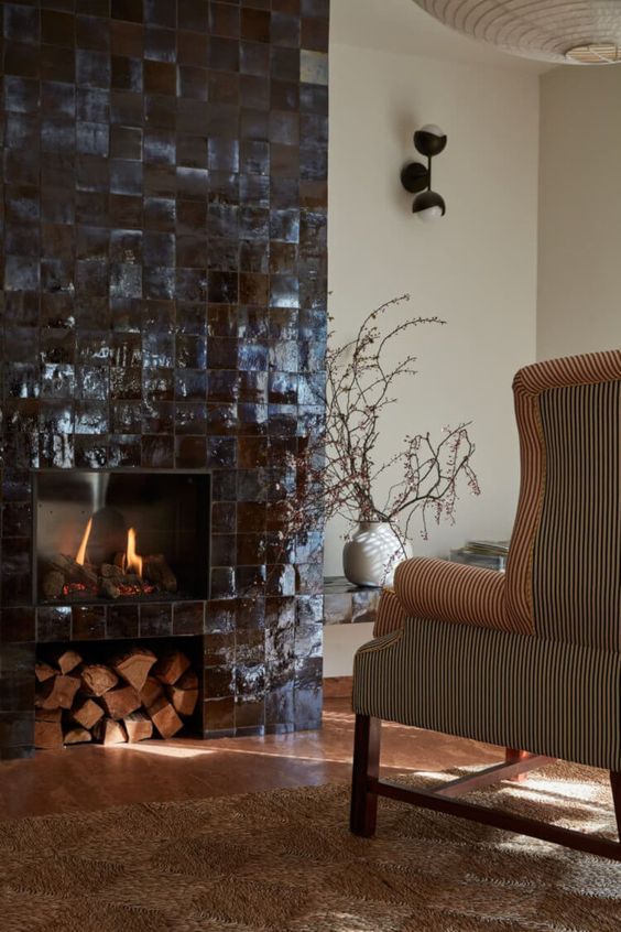 a fireplace clad with black Zellige tiles and a firewood niche is a stylish and eye-catchy idea due to its color and texture