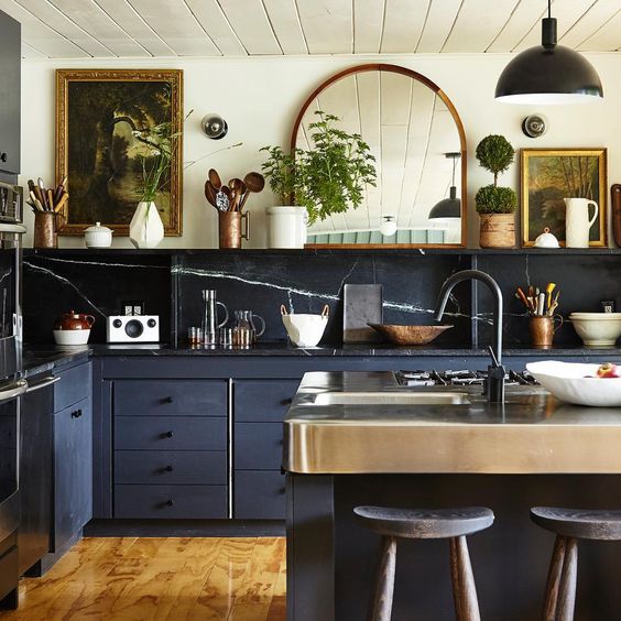 a gorgeous eclectic kitchen combining stone backsplash and countertops, navy cabinets and vintage artworks and a mirror