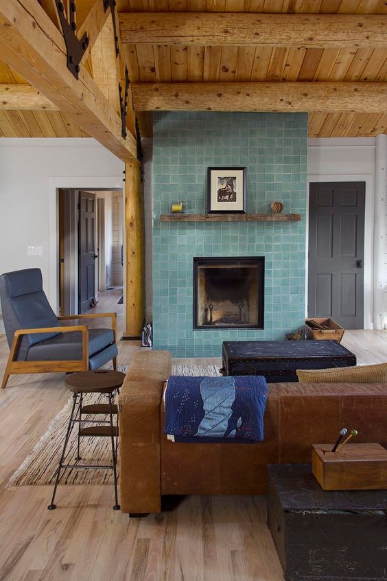 a living room with a stained ceiling, a leather sofa and a fireplace clad with aqua-colored Zellige tiles