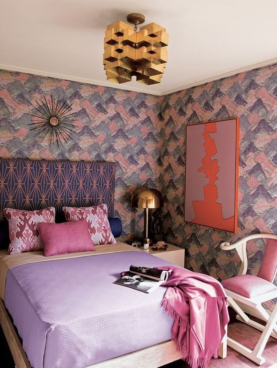 a lovely maximalist bedroom with brushstroke walls, a printed bed, pastel bedding, a pink chair, a gold sculptural chandelier