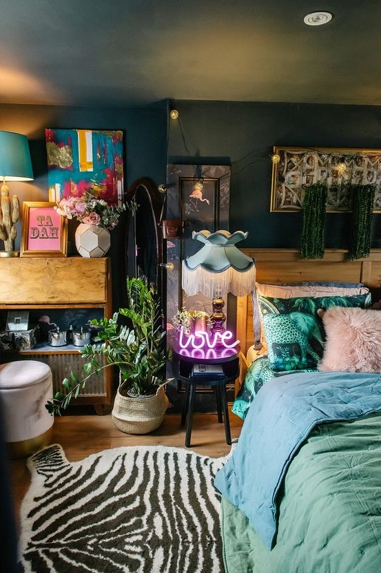 a lovely maximalist bedroom with dark walls and a ceiling, with mid-century modern furniture, pastel bedding, a potted plant, a neon light and colorful artworks