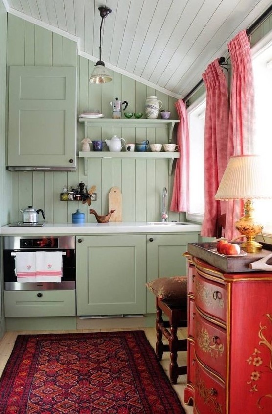 a lovely maximalist kitchen with olive green walls and a kitchen, a red dresser, a refined stool, pink curtains and a bright rug