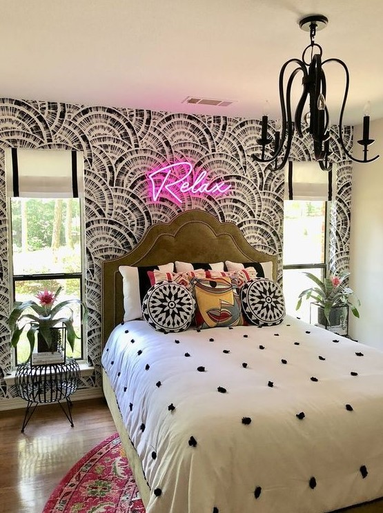 a maximalist bedroom with a printed accent wall, a green bed, bright bedding and a rug, a neon light and a black chandelier
