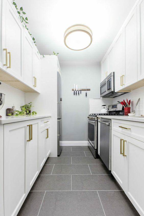 a modern farmhouse galley kitchen in white with gilded touches, a grey tile floor and a ceiling light is very stylish and cozy