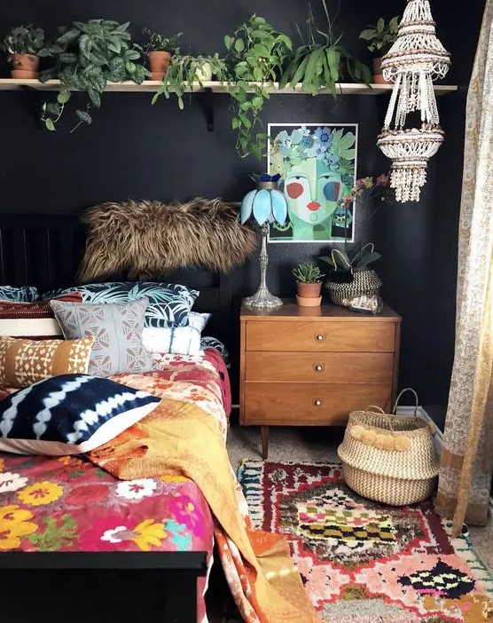 a moody eclectic bedroom with black walls, a bed with bright bedding, a logn shelf with potted plants, bright rugs and some decor