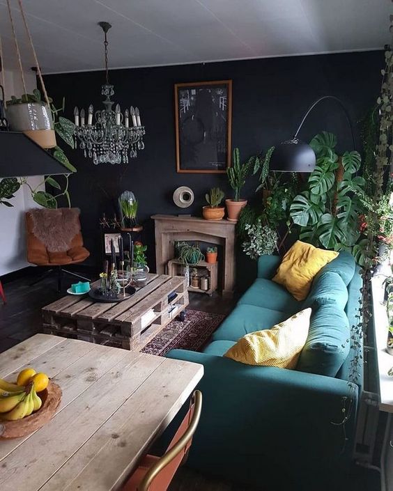 a moody eclectic living space with a teal sofa, a leather chair, colorful pillows, a crystal chandelier and a pallet coffee table