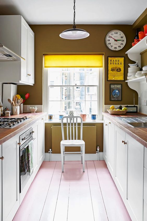 a pretty galley kitchen with mustard walls, white cabinets, butcherblock countertops and a pink floor, a pendant lamp