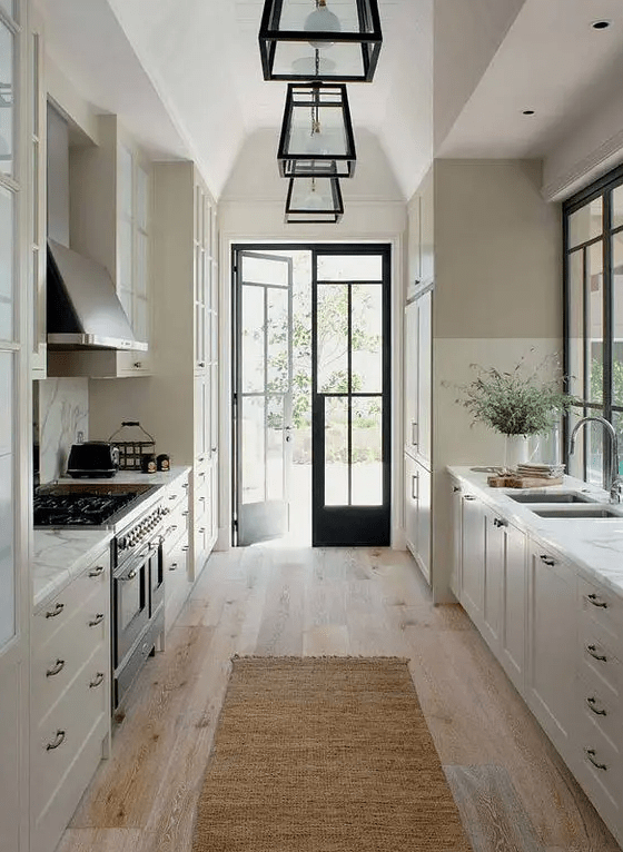 a refined white farmhouse kitchen with shaker cabients, black handles, a vintage style cooker and a hood, frame pendant lamps