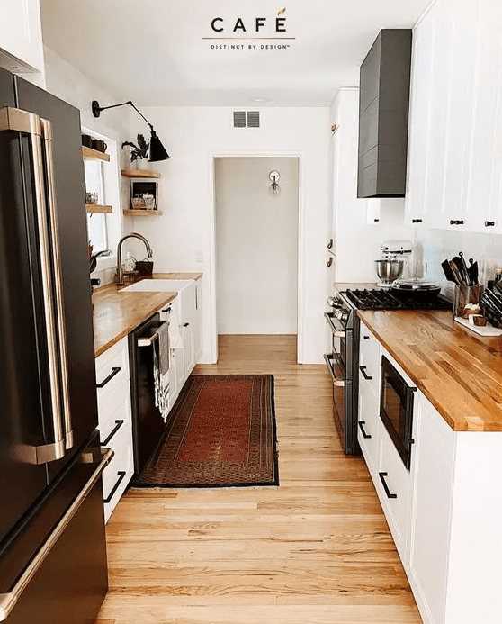 a small and cozy farmhouse kitchen with white cabinets, butcherblock countertops, black handles, open shelves and a black sconce