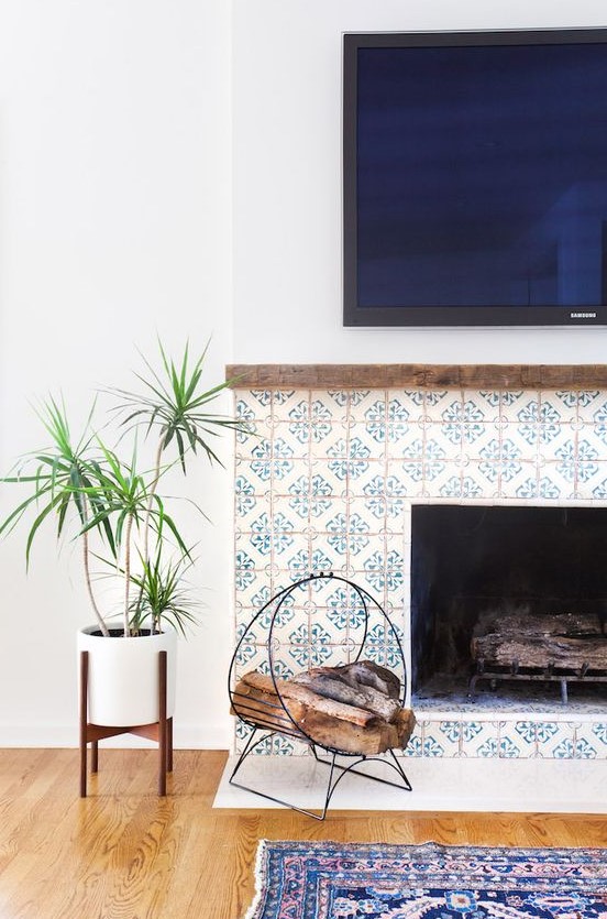 a stylish built-in fireplace clad with blue patterned tiles around it and with a delicate metal firewood stand next to it