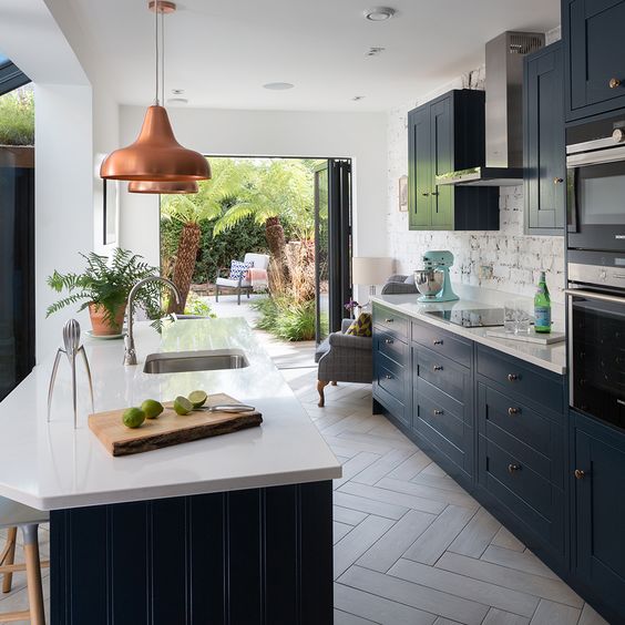 a stylish galley kitchen with navy cabinets and white stone countertops, copper pendant lamps and a brick backsplash