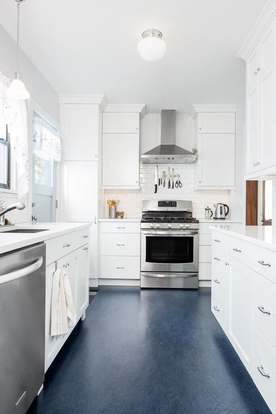 a tranquil neutral galley kitchen with white cabinets and countertops, a navy floor and stainless steel appliances