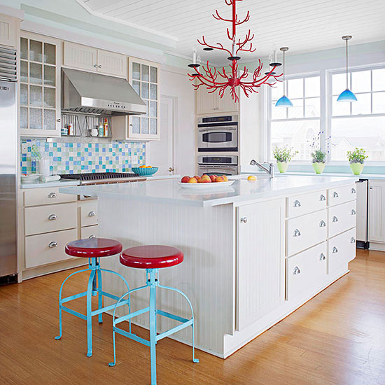 a white cottage kitchen spruced up with a glass tile backsplash, two toen stools and a unique red chandelier