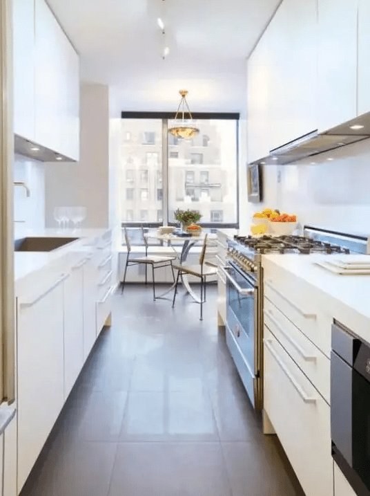 a white galley kitchen with sleek cabinets, built-in lights and appliances plus a dining zone at the window