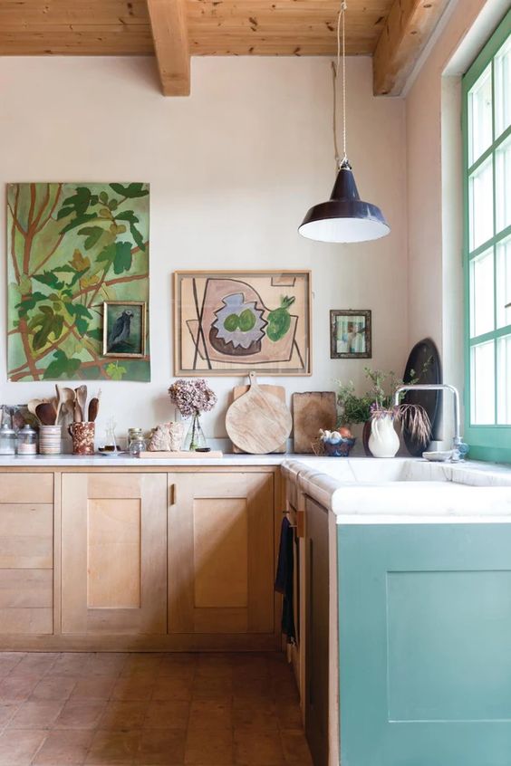 an airy eclectic kitchen with stained and pale green cabinets, a gallery wall, pendant lamps and some decor