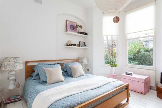 an eclectic bedroom with a modern wooden bed, a pink chest and stool, vintage-inspired lamps and modern built-in shelves