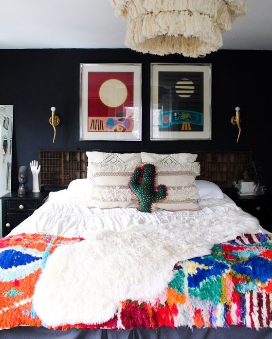 an eclectic bedroom with black walls, a bed with colorful boho bedding, a bold gallery wall, some decor and black nightstands