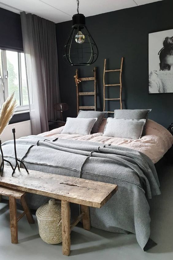an eclectic bedroom with black walls, a bed with grey and pink bedding, stained benches, ladders and an industrial lamp
