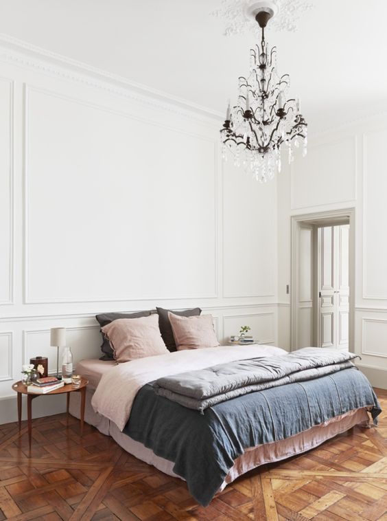 an eclectic bedroom with molding, a bed with pastel bedding, mismatching nightstands, a vintage chandelier