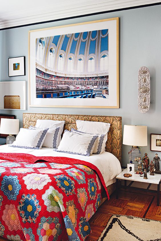 an eclectic bedroom with pale blue walls, a bed with a statement headboard, bright bedding, matching nightstands and lamps, some art