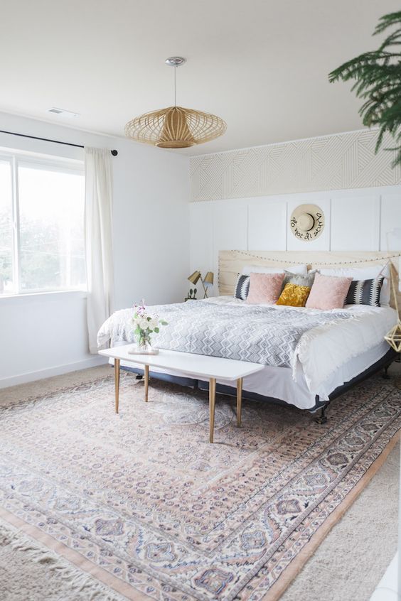 an eclectic bedroom with white paneling, a bed with printed bedding, a printed rug, a pendant lamp and greenery