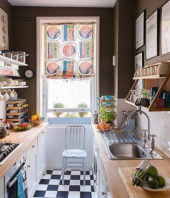 an eclectic galley kitchen with black walls, a checked floor, white cabinets with butcher block countertops and a colorful curtain