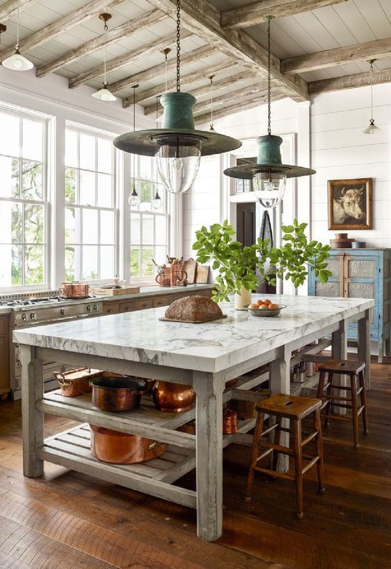 an eclectic kitchen with a shabby chic blue buffet, a large table that is a kitchen island, stained cabinets and stools, pendant lamps