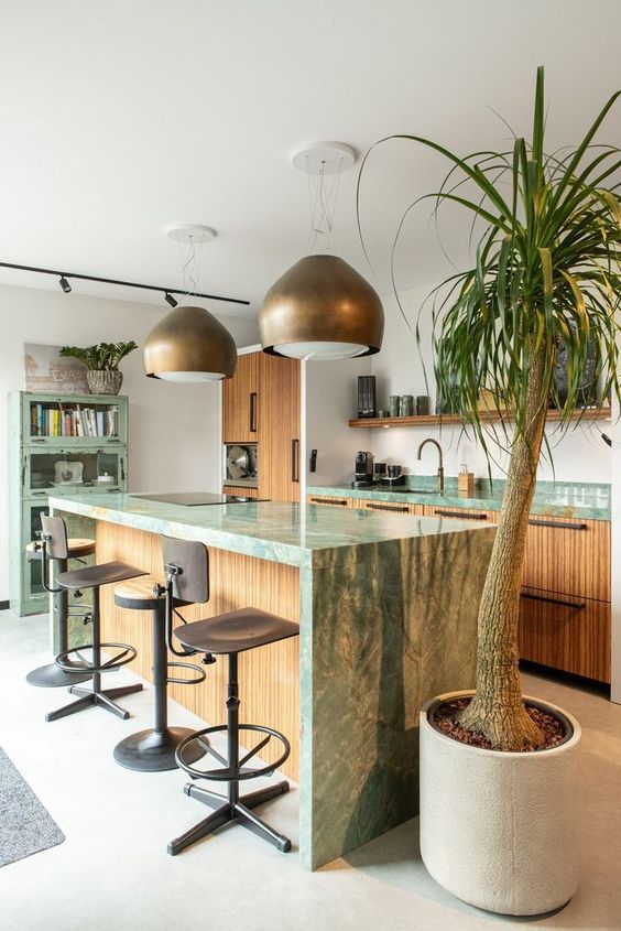 an eclectic kitchen with fluted cabinets and green marble countertops, a shabby chic green storage unit, brass pendant lamps and stools